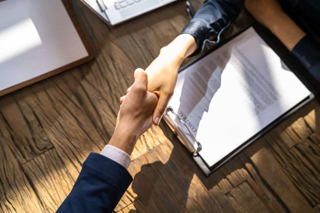 Friendly handshake between employee benefits broker and business owner over insurance agreement at a wooden desk, symbolizing trust and partnership in benefits group insurance services.